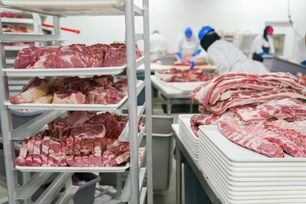 pexels-photo-7163991-7163991 A meat processing facility with workers handling meat cuts on trays, demonstrating industrial food production.